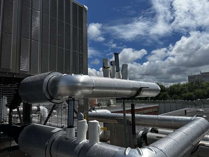 Insulated chiller condenser piping, gauges, and a cooling-tower coil on a flat roof.