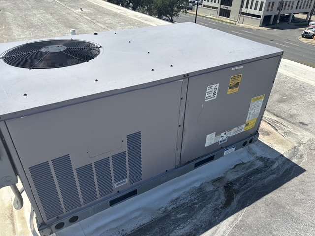 Side of a packaged commercial rooftop air conditioner sitting on a curb above a city street.