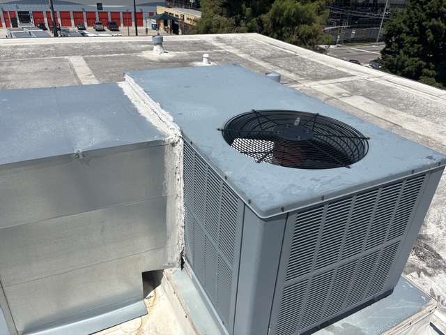 Packaged rooftop air conditioner beside a duct curb sealed to the unit on a commercial roof.