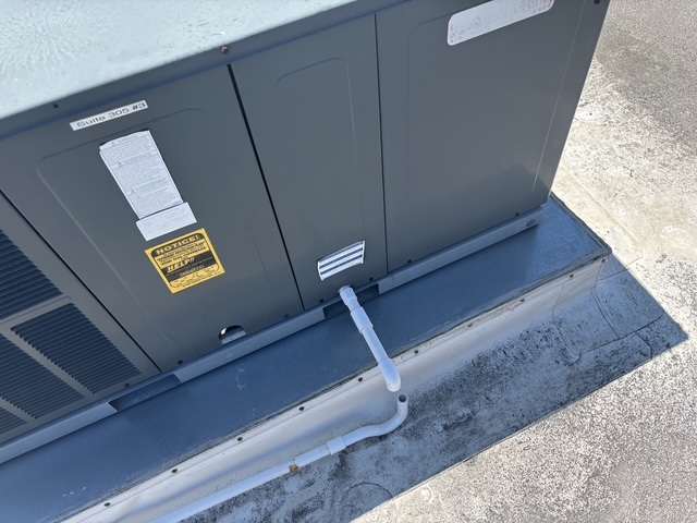 Close view of a commercial rooftop cabinet, roof curb, and condensate drain on a flat roof.