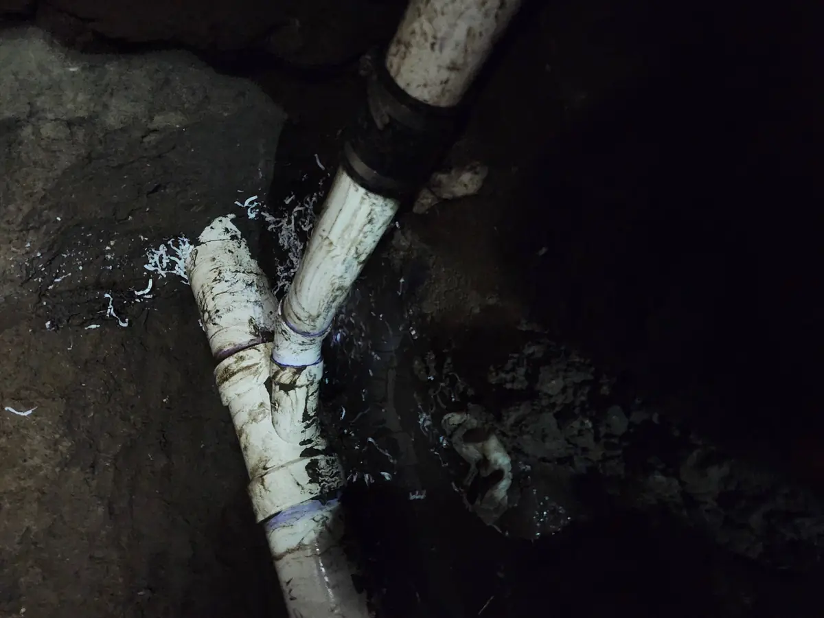 New PVC pipe and fittings in a muddy New Orleans plumbing excavation after repair
